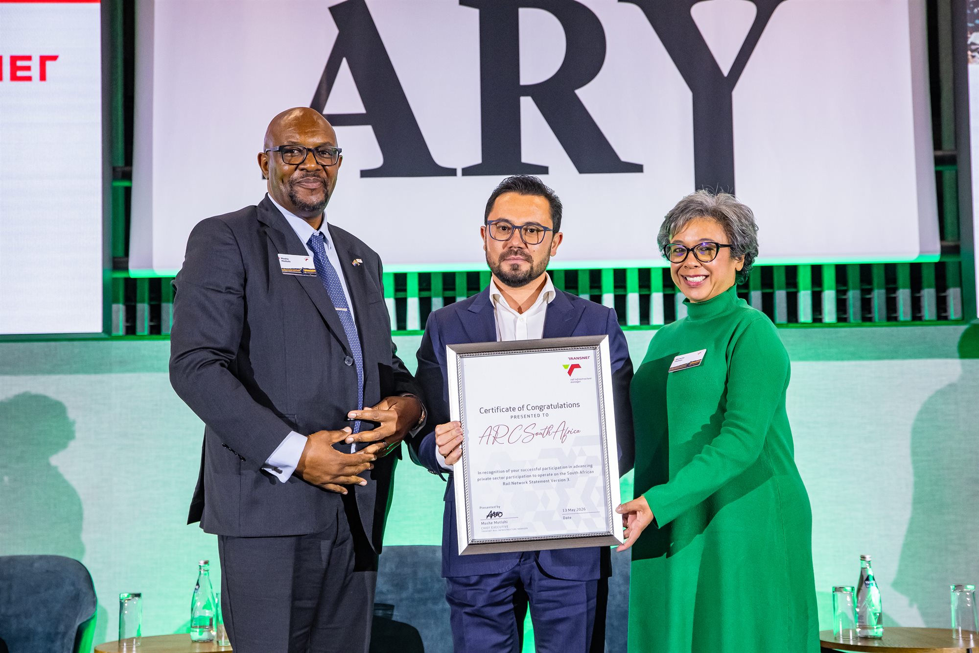 Award recipient holding a certificate between two presenters on stage