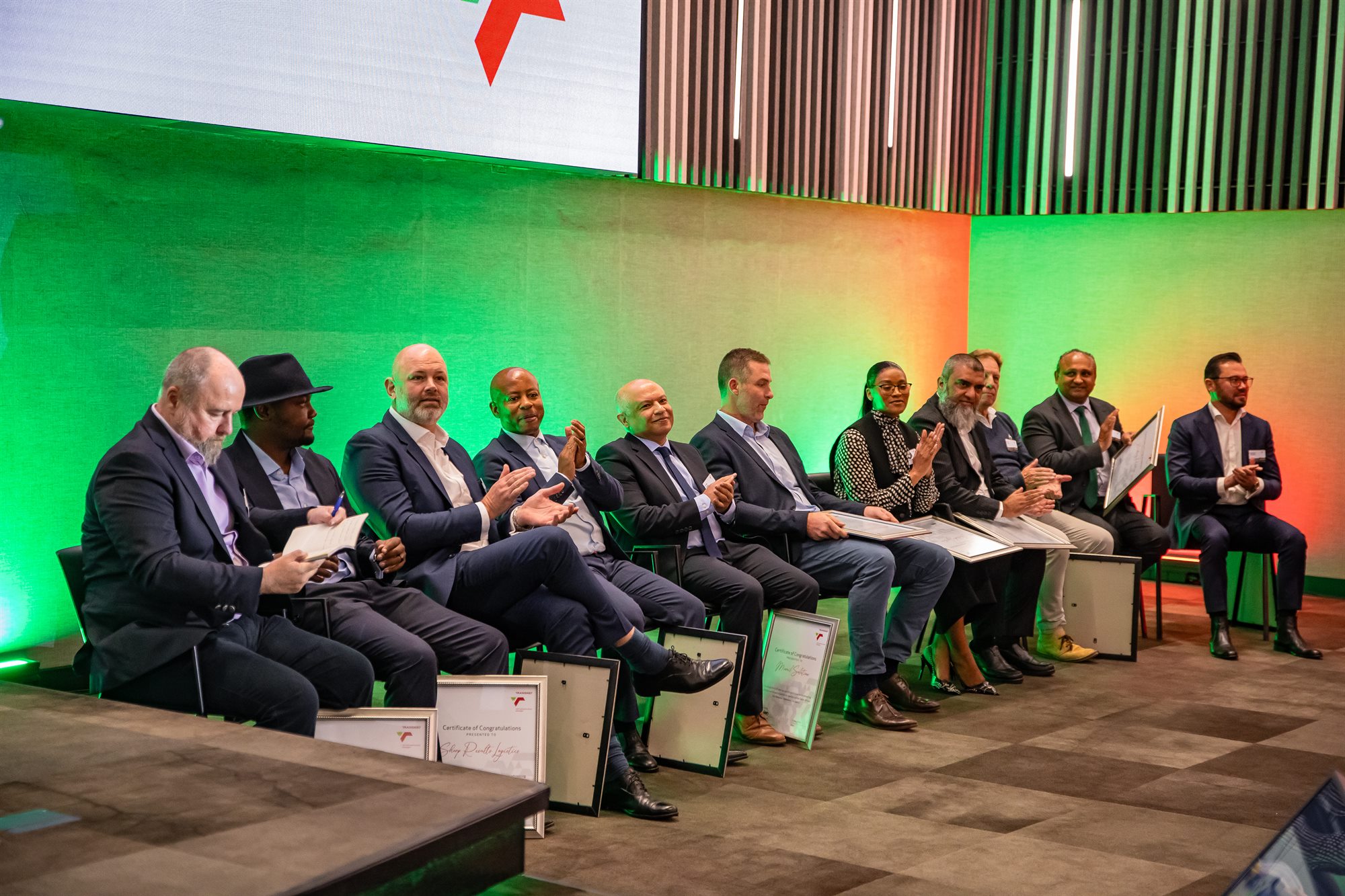Panel of guests seated on stage applauding at a corporate awards evening