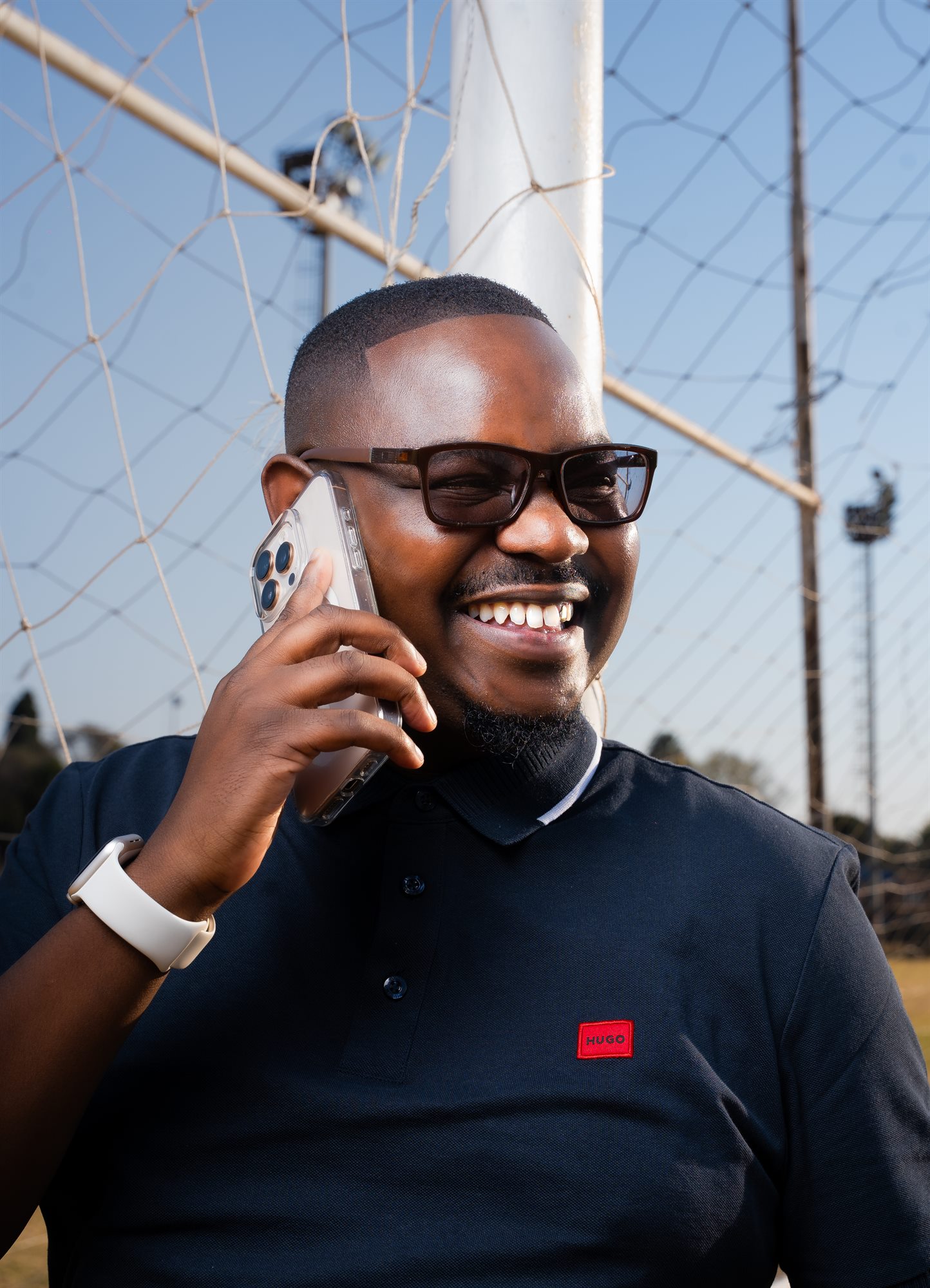 Portrait of a man laughing on a phone call at a floodlit sports field