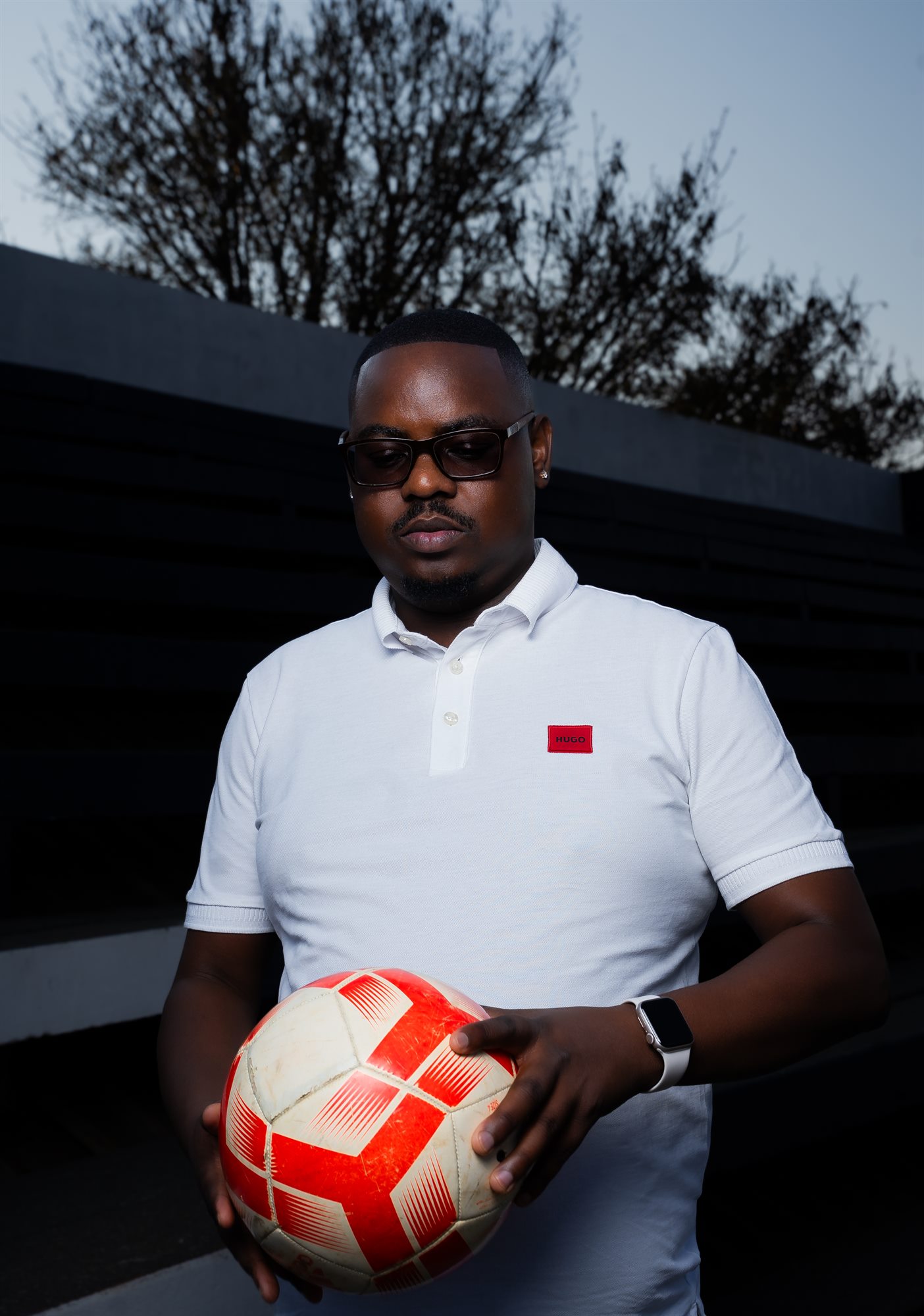Portrait of a man in a white polo shirt holding a soccer ball at dusk