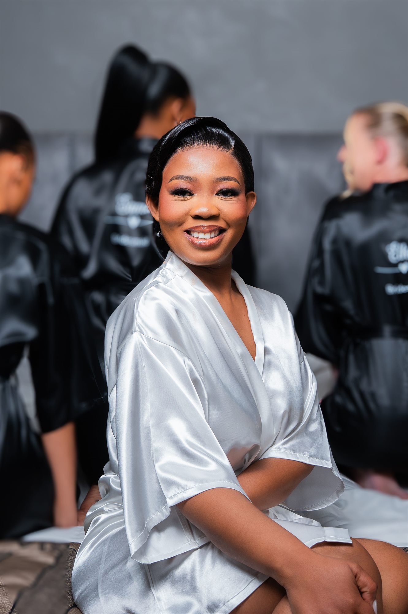 Bride in a satin robe smiling while getting ready with her bridal party