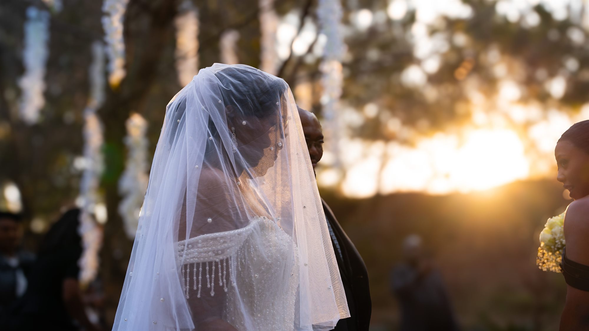 Bride in a beaded veil backlit by the setting sun